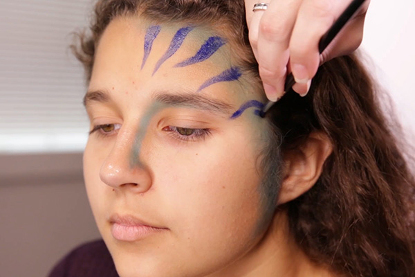 You apply the acrylic blue paint for wavy stripes, step 3 of the Avatar Face Paint Tutorial.