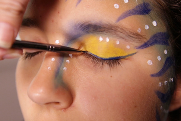 You apply the acrylic blue paint for winged eye liner, step 8 of the Avatar Face Paint Tutorial.